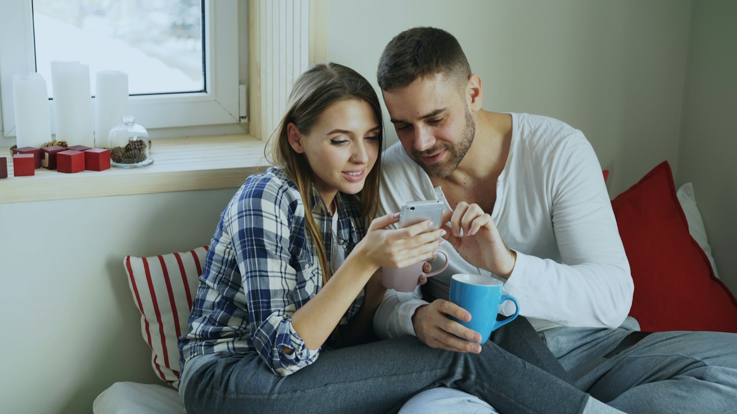 Couple looking at a smartphone while holding mugs.